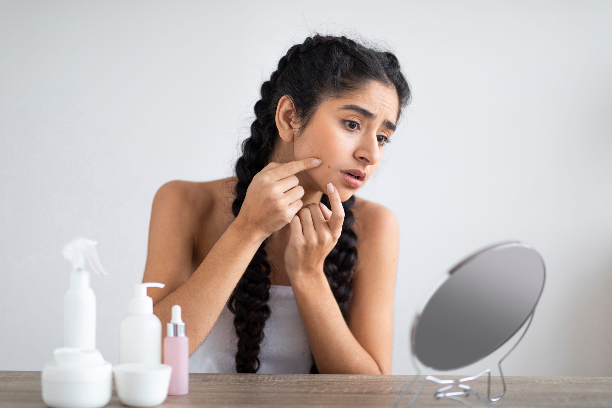 An Indian woman with braided hair looking in a mirror and checking acne, a common PCOS symptom.