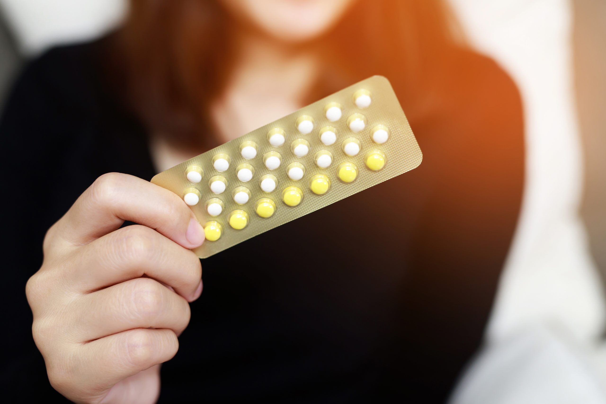 A woman holding a blister pack of hormonal pills, commonly used as medicine for PCOS and irregular periods.