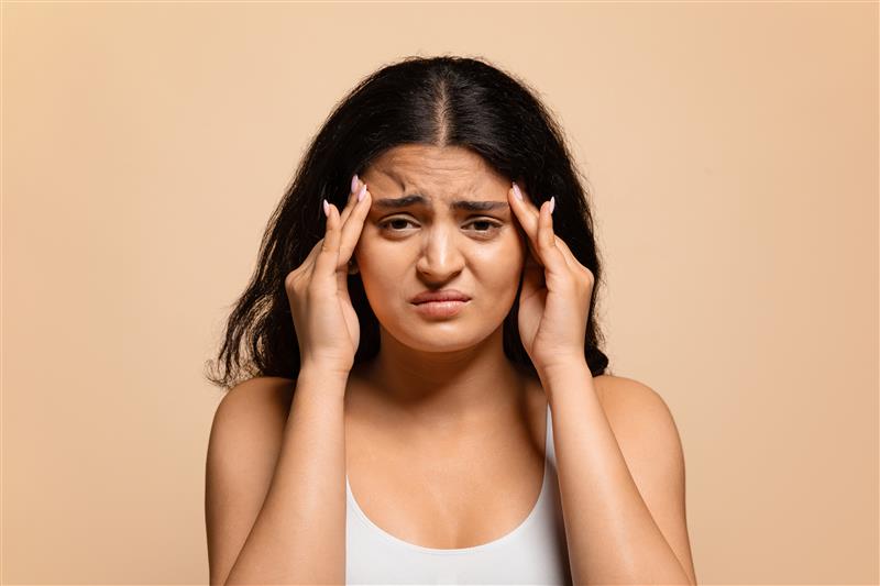 Young Indian woman holding her temples with stress and headache, common with PCOS symptoms and irregular periods.